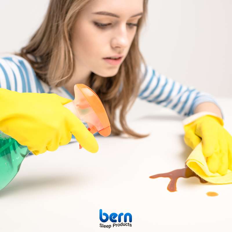 یک تشک با لکه خون که با دستمال تمیز و محلول لکه‌بر در حال پاک شدن است.